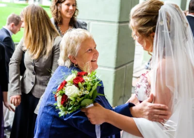Braut begruesst Gast mit Blumenstrauss bei Hochzeitsreportage im Kloster Benediktbeuern, festgehalten von Hochzeitsfotograf.
