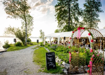 Hochzeitsfeier im Kleinen Seehaus Starnberger See mit festlich geschmücktem Blumenbogen und Gästen im Festzelt.