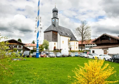 Kirchliche Trauung in Schaftlach, Kirche mit Maibaum, versammelt für Hochzeitsreportage, umgeben von Autos und Häusern.
