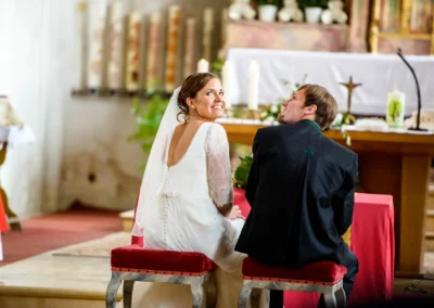 Brautpaar sitzt bei kirchlicher Trauung in Valley auf roten Stuehlen, rueckwaerts zur Kamera in einer Kirche.