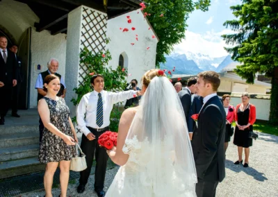 Hochzeitsfoto in Oberbayern: Brautpaar vor Kirche, Gaeste werfen Rosenblaetter in Garmisch-Partenkirchen.