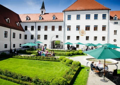Hochzeitsfeier im Garten des Kloster Seeon mit Gaesten unter gruenen Sonnenschirmen. Hochzeitsfotografie Chiemgau.