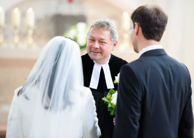 Brautpaar mit Pfarrer bei kirchlicher Trauung in Aufkirchen. Hochzeitsfoto mit Braut in weissem Schleier.