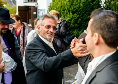 Hochzeitsgast gratuliert Brautpaar in St. Vitus Gilching bei kirchlicher Trauung im Freien, Hochzeitsfoto.