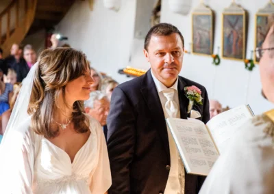 Brautpaar bei kirchlicher Trauung in Sankt Peter, München. Hochzeitsreportage zeigt Zeremonie mit Priester und Gästen.