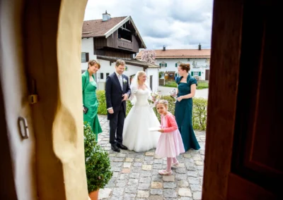 Brautpaar mit Gaesten vor Kirche in Schaftlach. Kirchliche Trauung bei Hochzeit. Hochzeitsreportage in Bayern.