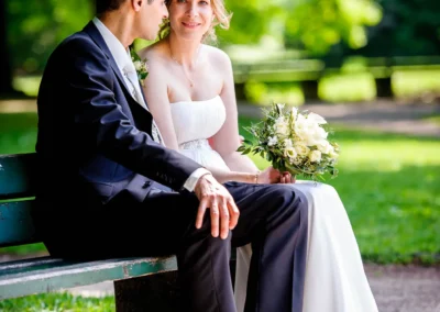 Brautpaar sitzt lachend auf einer Parkbank in Muenchen. Hochzeitsportraits im Luitpoldpark München.
