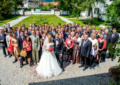 Brautpaar und Hochzeitsgesellschaft posieren bei Sonnenschein in Garmisch-Partenkirchen für Gruppenfoto. Hochzeitserinnerung.