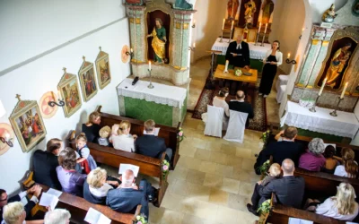 Kirchliche Trauung auf Gut Thurnsberg, Brautpaar sitzt vor Altar, Gäste in Kirchenbänken, Hochzeitsfotografie.