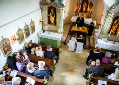 Kirchliche Trauung auf Gut Thurnsberg, Brautpaar sitzt vor Altar, Gäste in Kirchenbänken, Hochzeitsfotografie.