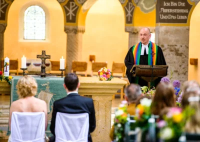 Kirchliche Trauung in Schwabing, Pfarrer vor Altar mit Brautpaar, umgeben von Kerzen und Blumen, Hochzeitsfoto.