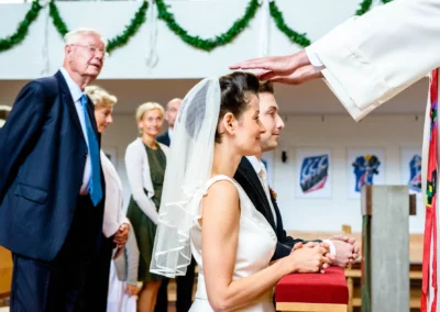 Brautpaar wird bei der kirchlichen Trauung in Feldafing gesegnet, Gäste im Hintergrund lächeln. Hochzeitsfotografie.