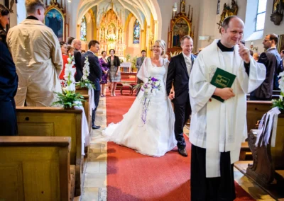 Brautpaar verlässt Kirche nach Trauung in Pasing, begleitet von Gästen. Hochzeitsfotograf aus München.