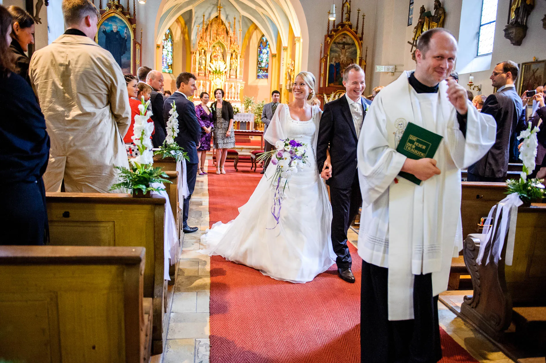 Brautpaar verlässt Kirche nach Trauung in Pasing, begleitet von Gästen. Hochzeitsfotograf aus München.