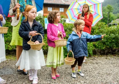 Kinder mit Koerben bei einer Hochzeitsfeier nahe Walchensee, umgeben von Regenschirmen und Natur. Hochzeitsfoto.