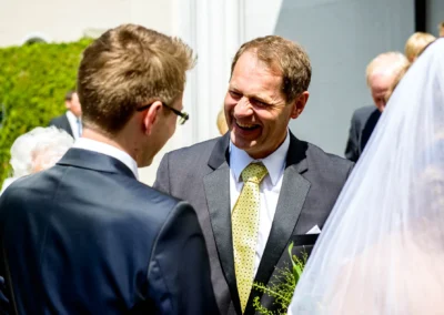 Ein herzliches Gespraech bei der Hochzeit vor der Friedenskirche Starnberg, festgehalten als Teil der Hochzeitsreportage.