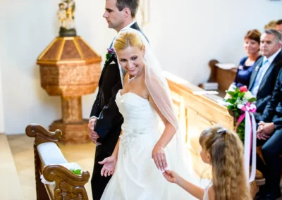 Brautpaar in Kirche bei Hochzeit, Blumenmaedchen gibt etwas der Braut, Hochzeitsfotografie in Taufkirchen bei Muenchen.