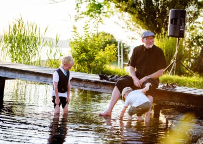 Ein Vater mit zwei Kindern spielt im Wasser an einem Steg, aufgenommen bei einer Hochzeit am Starnberger See.