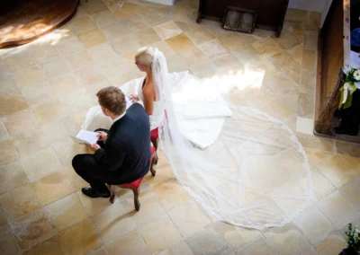 Brautpaar sitzt in der Kirche bei der Trauung in Bernried, Hochzeitsfoto mit Fokus auf Brautkleid Details.