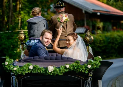 Brautpaar in Kutsche bei Hochzeit, Braut grinst, nahe Spitzingsee, Hochzeitsfotografie, fröhliche Szene im Grünen.
