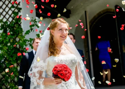 Braut mit rotem Blumenstrauss und Schleier, umgeben von fallenden Rosenblaettern bei einer Hochzeit in Garmisch-Partenkirchen.