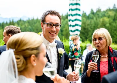 Hochzeitsfoto nahe Tegernsee: Fröhliche Gäste bei der Hochzeit im Gespräch, halten Sektgläser.