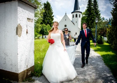 Brautpaar auf einem Weg vor Kirche in Garmisch, Braut in weissem Kleid mit Blumenstrauss, Hochzeitsreportage.