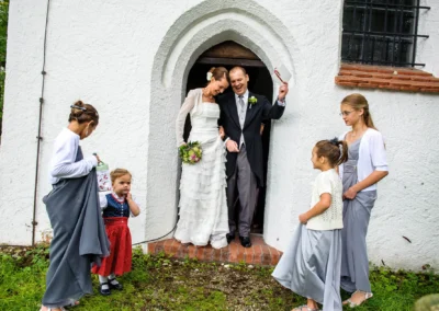 Brautpaar und Kinder verlassen Kirche nach Trauung bei Hochzeit auf Gut Thurnsberg, Hochzeitsfotografie in Oberbayern.