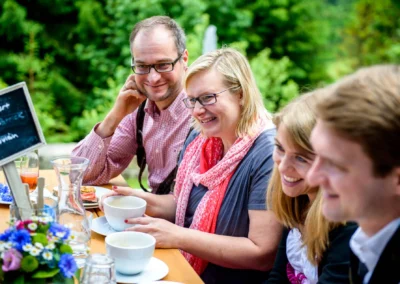 Gruppe lacht bei Kaffee auf Hochzeit im Sillberghaus. Hochzeitsreportage in Bayrischzell zeigt Freude im Freien.
