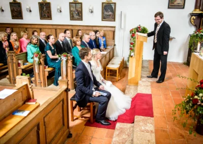 Brautpaar bei kirchlicher Trauung in Schaftlach, fotografiert vom Hochzeitsfotografen, umgeben von Gaesten in der Kirche.