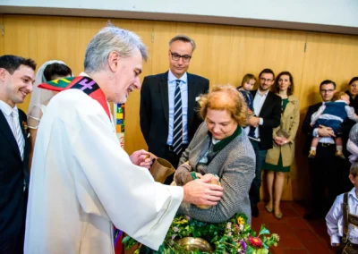 Priester segnet Kind bei kirchlicher Trauung in Feldafing. Hochzeitsreportage am Starnberger See. Feiernde Gäste.