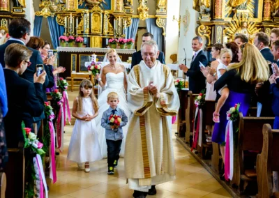Priester mit Brautpaar und Blumenkindern bei kirchlicher Trauung in Taufkirchen nahe München, Hochzeitsfotografie.