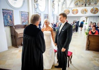 Brautpaar vor Altar bei kirchlicher Trauung in Bernried. Hochzeitsfotografie mit Gästen im Hintergrund.