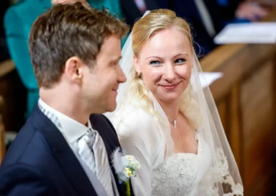 Brautpaar laechelt sich waehrend der kirchlichen Trauung in einer Kirche in Schaftlach an. Hochzeitsfoto mit Freude.