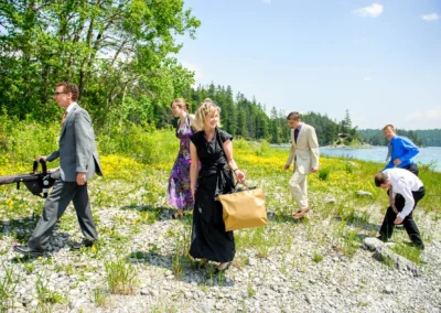Gäste spazieren bei Hochzeit am Eibsee entlang, umgeben von blühenden Wiesen und klarem Wasser. Hochzeitsreportage.