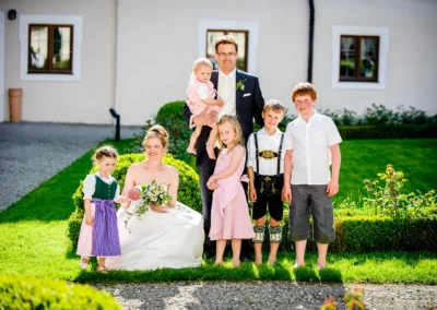 Familienfoto bei einer Hochzeit im Kloster Seeon. Braut laechelt mit Kindern im Garten. Hochzeitsfotografie in Oberbayern.