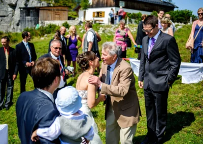 Gäste bei einer Hochzeitsfeier im Freien bei Aschau im Chiemgau, Braut und älterer Herr umarmen sich.