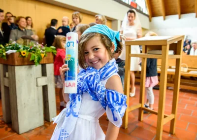 Mädchen lächelt mit Kerze in einer Kirche bei Hochzeit in Feldafing; Hochzeitsfotografie im Reportagestil am Starnberger See.