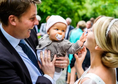 Mann haelt Baby bei kirchlicher Hochzeit in Muenchen, Braut laechelt, Hochzeitsfotograf Pasing.