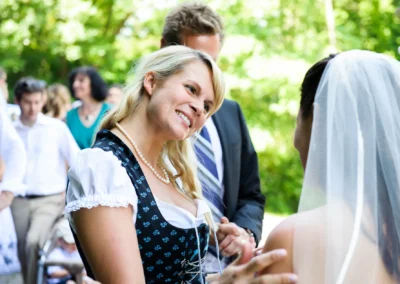 Lachende Frau im Dirndl spricht mit Braut bei Hochzeit in Wolfratshausen. Hochzeitsfotografie in Oberbayern.