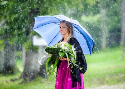 Frau mit Blumenstrauss und blauem Regenschirm im Regen bei einer Hochzeitsreportage in Uffing am Staffelsee.