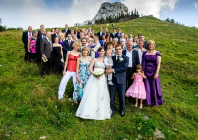 Große Hochzeitsgesellschaft auf Wiese nahe Kampenwand mit Brautpaar im Vordergrund. Hochzeitsfoto Oberbayern.