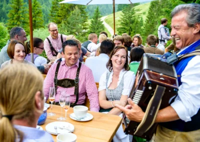 Gäste feiern Hochzeit im Almbad-sillberghaus bei Bayrischzell mit Akkordeonmusik im Freien. Hochzeitsfotografie.