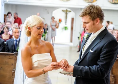 Braut steckt Ring an Bräutigams Finger in Kirche bei Hochzeit in Bernried am Starnberger See. Hochzeitsfotografie.