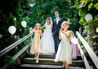 Hochzeitsfoto von Brautpaar und Kindern beim Seifenblasen im Freien, Sprengenöder Alm nahe Starnberger See.