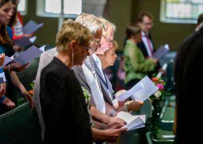 Gäste bei kirchlicher Trauung in München Schwabing, halten Programme in der Kirche. Hochzeitsfoto von Hochzeitsfotograf.