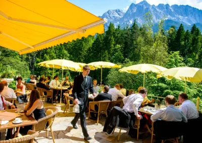 Gäste bei Hochzeit auf Terrasse in Grainau mit gelben Sonnenschirmen und Blick auf Berge. Hochzeitsreportage.