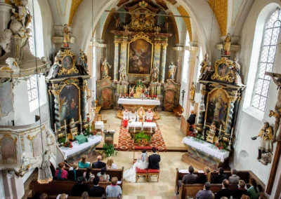 Kirchliche Trauung in Pfarrkirche Sankt Michael, Arget. Brautpaar vor Altar, umgeben von Gästen. Hochzeitsreportage.