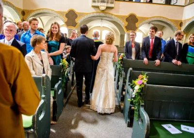Brautpaar schreitet durch Kirche bei Trauung in Schwabing, Gaeste schauen, Hochzeitsreportage in Muenchen.