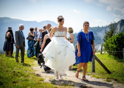 Braut in weissem Kleid mit Hochzeitsgesellschaft auf dem Weg bei der Kampenwand. Hochzeitsfotografie im Chiemgau.